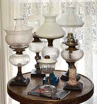 Photo of six early kerosene table lamps with burners and shades.